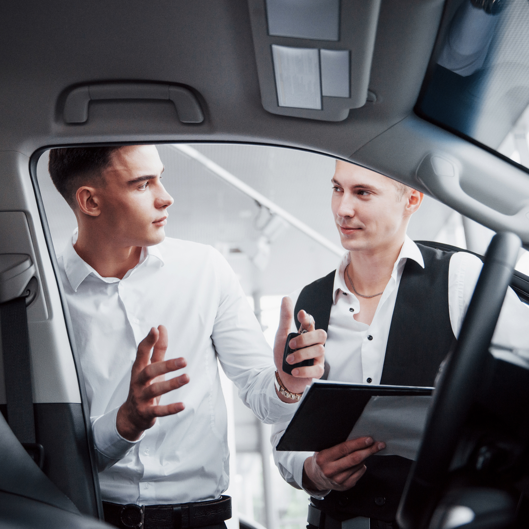 b2-ride-Two men stand in the showroom against cars. Close-up of a sales manager in a suit that sells a car to a customer. The seller gives the key to the customer.